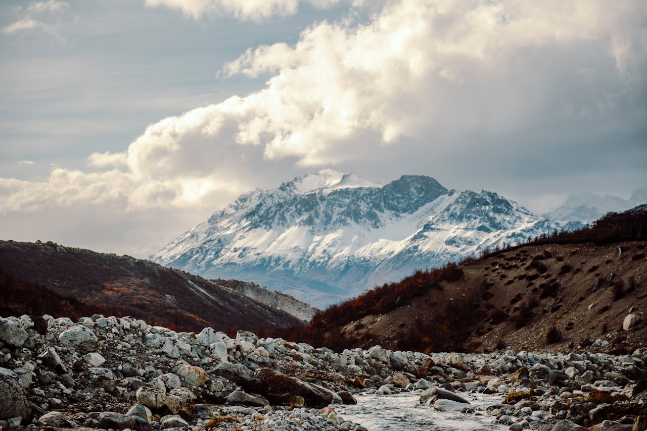 services-01 Snow-capped mountains rise majestically over rocky terrain under a dramatic sky.